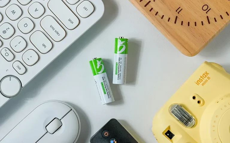 Baterai AA rechargeable di meja kerja bersama keyboard, mouse, dan perangkat elektronik harian